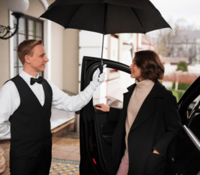 Chauffeur holding an umbrella for a woman stepping out of a car